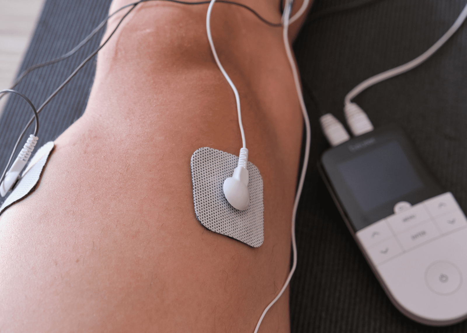 Pierna con electrodos conectados a un electroestimulador muscular, mostrando una sesión de recuperación y fortalecimiento muscular tras el ejercicio.